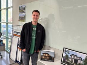 Modular home builder Scott Voulgaris of Mountain View, CA-based Aro homes poses in front of pictures of his firm’s modular homes.