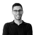 Black and white headshot of Andrew Staniforth, wearing a black shirt and glasses. 