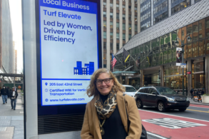 A woman stands in front of an electric sign on a city street.