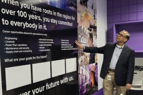 A man in business attire stands in front of a wall mural about career opportunities and a purple wall.