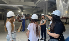 Women wearing white hardhats visit an active jobsite for the construction of a building.