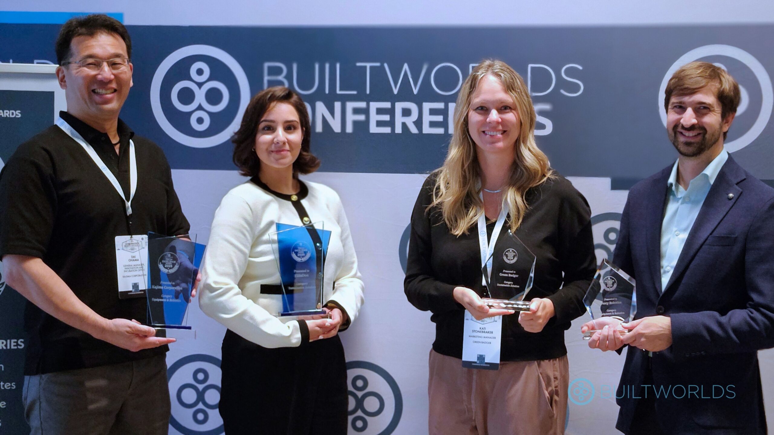 Two men and two women pose in front of a step and repeat backdrop holding glass awards. 