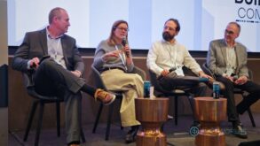 Four business people (three men and one woman) speak on a panel in front of an audience.