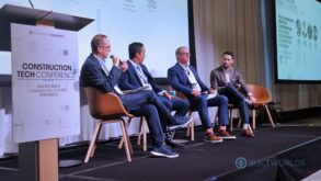 Four men in suits sit on a stage and talk into microphones. A sign saying they are at BuiltWorlds 2025 Construction Tech Conference is in the foreground.