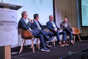 Four men in suits sit on a stage and talk into microphones. A sign saying they are at BuiltWorlds 2025 Construction Tech Conference is in the foreground.