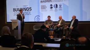 Four men address each other on a business panel