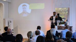 A man in a suit stands at a podium addressing a crowd.