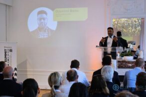 A man in a suit stands at a podium addressing a crowd.