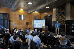 A man in a blue sweater presents to a room of business people