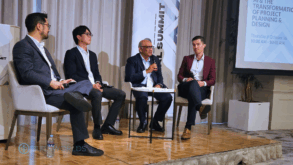 Four men sit on a raised podium speaking at a business conference.