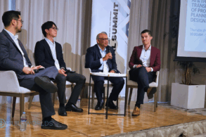 Four men sit on a raised podium speaking at a business conference.