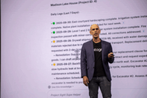 Man in blazer and datagrid shirt give presentation in front of large screen