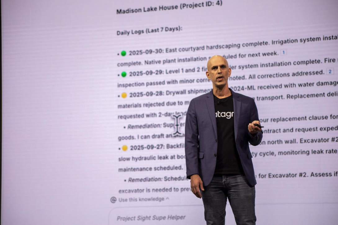 Man in blazer and datagrid shirt give presentation in front of large screen