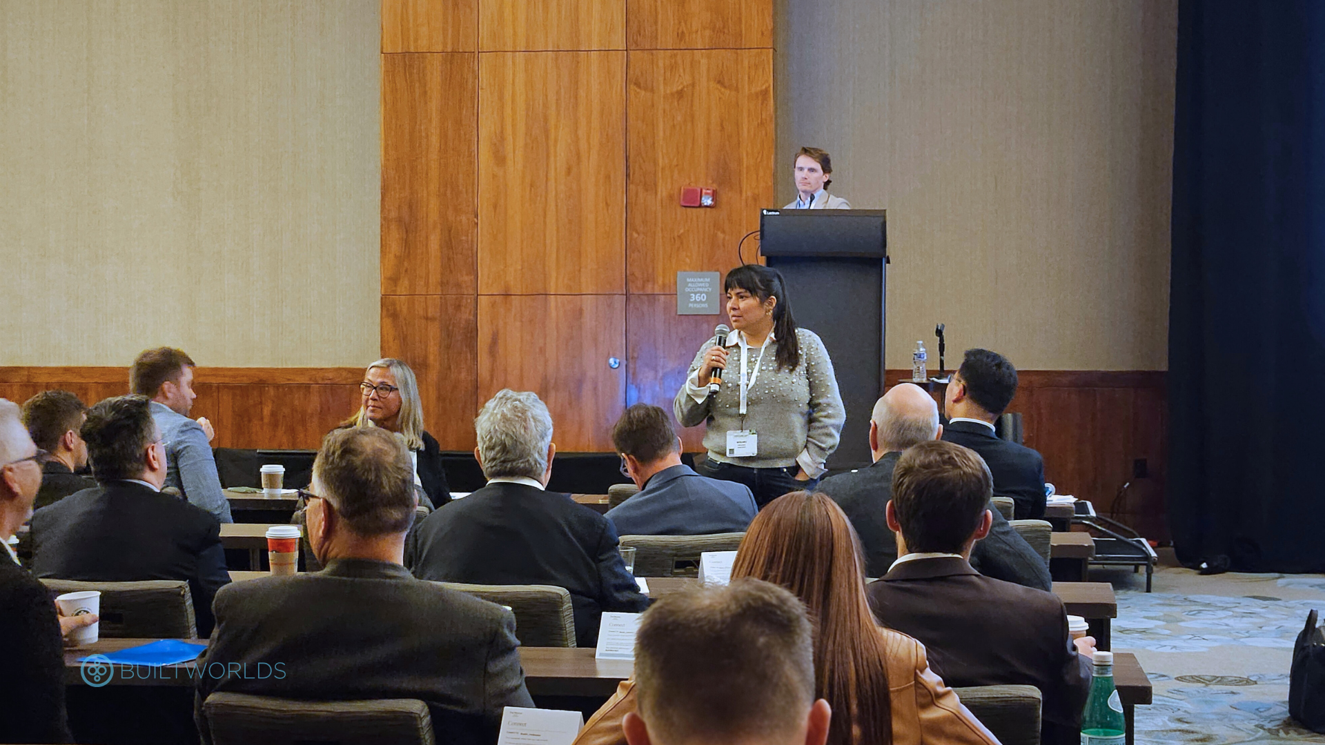 A woman speaks into a microphone from the audience at a business conference