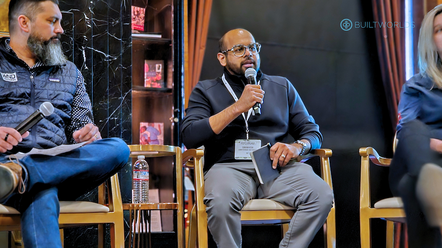 man sitting on stage at a conference speaking into microphone
