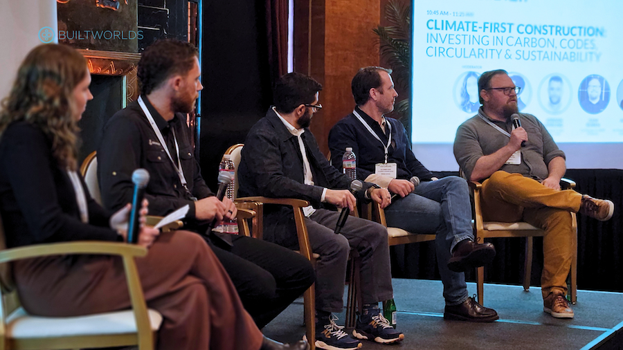 five people on stage at a conference, sitting, speaking into microphones